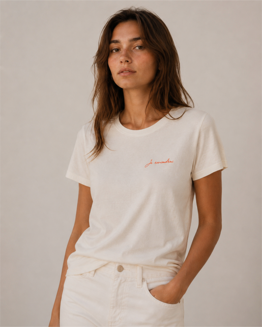 Woman wearing cream t-shirt with coral "Je reviendrai" script detail, paired with white jeans — muzee coastal aesthetic