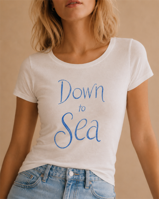 Woman wearing a white summer T-shirt with a blue hand-drawn “Down to Sea” print, close-up editorial product photo.